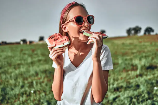 Photo of Sexy girl in red sunglasses holds a cut watermelon in her hands.