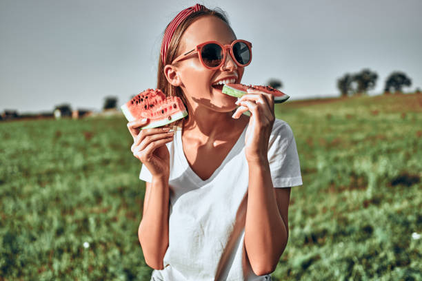 garota sexy de óculos escuros vermelhos segura uma melancia cortada em suas mãos. - women eating fruit food - fotografias e filmes do acervo