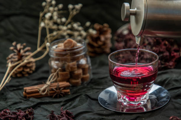 istock Roselle tea (Jamaica sorrel, Rozelle or hibiscus sabdariffa ) is poured from a kettle into glass cup  with dry roselle and brown cane sugar cube. 1207155280