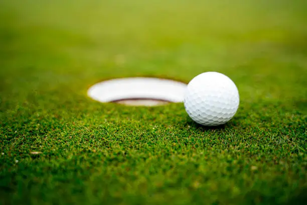 Golf ball on the green next to the hole