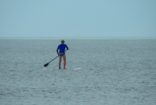 Photo taken on 2/15/2020 at 11:12 am at Praia do Cassino, Rio Grande, RS, Brazil.Unfamiliar man enjoying and exercising on his stand up board in the calm sea at Casssino beach.
