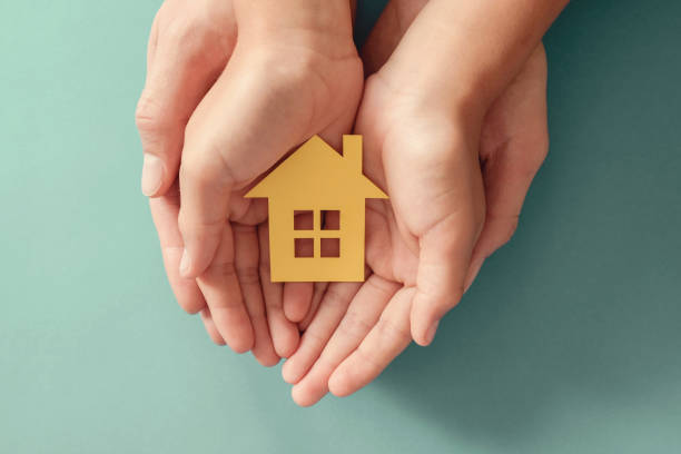 Hands holding yellow paper house on blue background, family home, homeless shelter housing and home protecting insurance, mortgage concept, foster home care Hands holding yellow paper house on blue background, family home, homeless shelter housing and home protecting insurance, mortgage concept, foster home care emergency shelter photos stock pictures, royalty-free photos & images