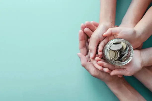 Photo of child and parent hands holding money jar, donation, saving, family finance plan concept