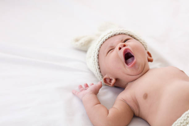 un bébé d’un mois dort sur un matelas blanc. bébé bâillant quand ils se sentent somnolents. - baby yawning asian ethnicity newborn photos et images de collection