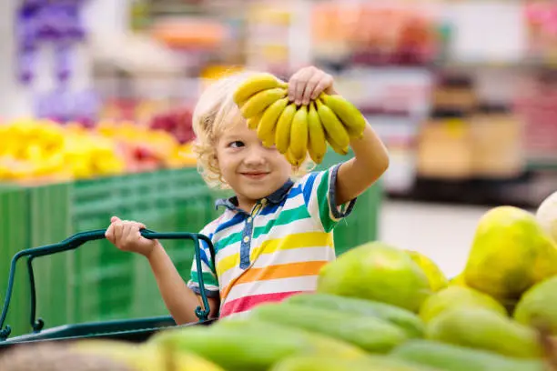 Photo of Child in supermarket. Kid grocery shopping.