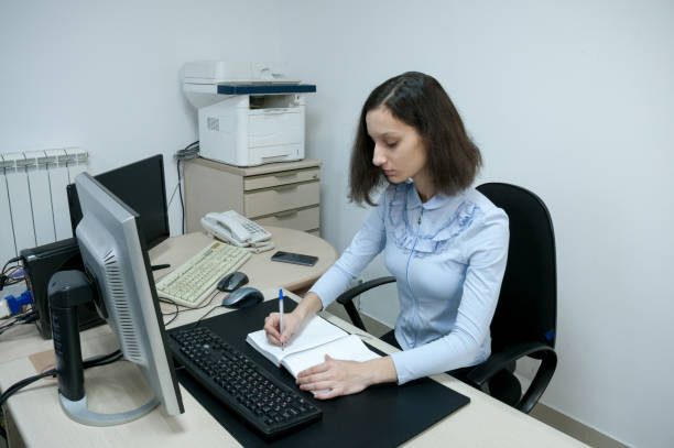 istock Brunette girl makes notes in a notebook in the office at the computer 1207175210