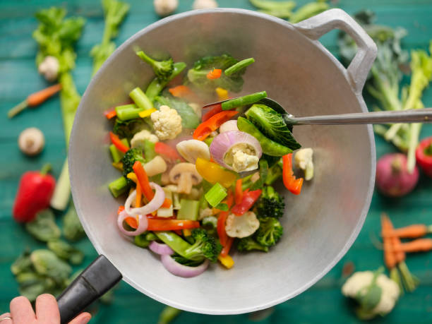 revuelva freír y saltear una variedad de verduras frescas de mercado de colores en un wok caliente humeante con verduras sobre un fondo de mesa de madera de color turquesa debajo del wok. - contrasts viewpoint wood wood panelling fotografías e imágenes de stock