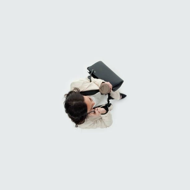 caucasian mid adult women business person walking in front of white background in the office wearing businesswear and holding purse and using mobile phone - 13603 imagens e fotografias de stock