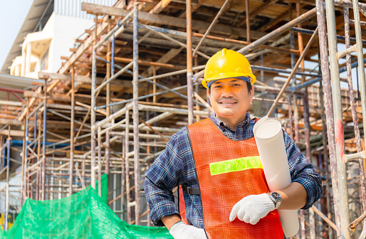 Engineer man checking and planning project at construction site, Smiling man holding paper blueprint and looking to camera