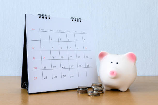 calendar with days and piggybank on wood table - stock market data insurance savings finance imagens e fotografias de stock