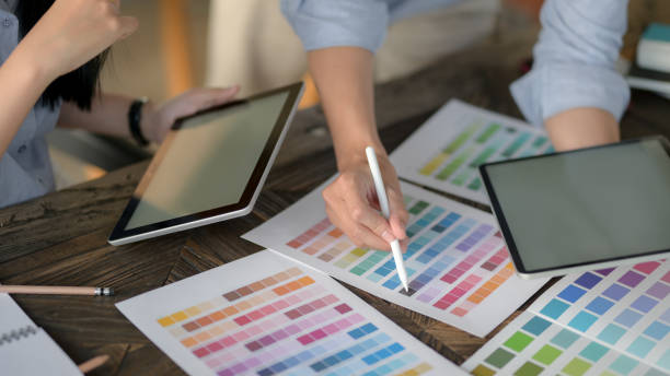 istock Close up view of designer team using digital tablet while choosing colour on colour swatch on vintage wooden table 1207185544