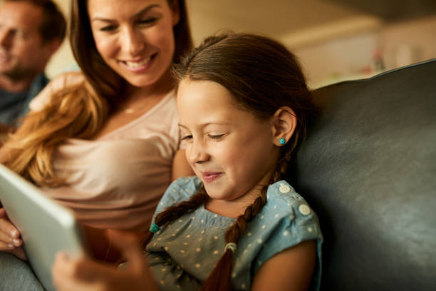 Browsing a world of educational apps Shot of an adorable little girl using a digital tablet while relaxing with her family at home free girl download stock pictures, royalty-free photos & images