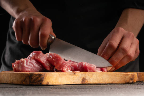 istock Chef cuts fresh pork for cooking close-up. On a black background. Cooking and Recipe Book. Delicious and wholesome food. 1207199263