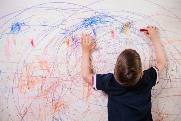 el niño dibuja en la pared con un crayón. el niño se dedica a la creatividad en casa - paintings child house childhood fotografías e imágenes de stock