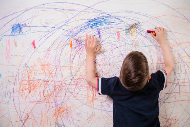 il bambino disegna sul muro con un pastello. il ragazzo è impegnato nella creatività a casa - paintings child house childhood foto e immagini stock