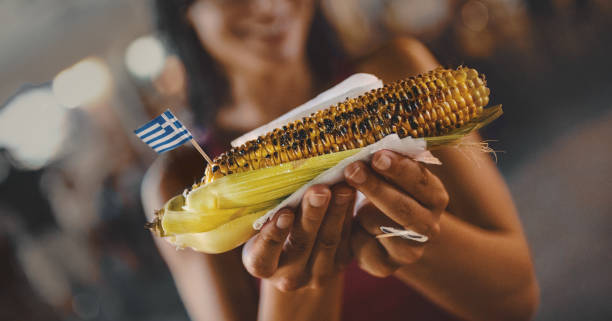 Unrecognizable young woman holding a grilled corn with Greek flag on it.