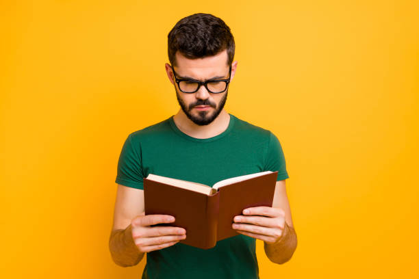 istock Portrait of focused college student guy hold read textbook learn information for study project wear spectacles good looking clothes isolated over yellow color background 1207210871