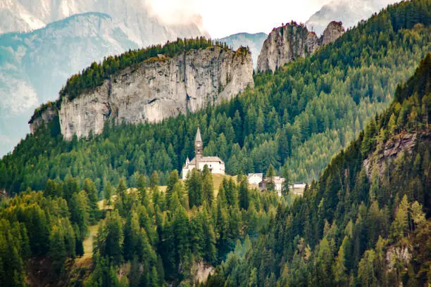 Photo of Small church with a chapel on a background of a mountain forest in the Italian Dolomite Alps, Italy.