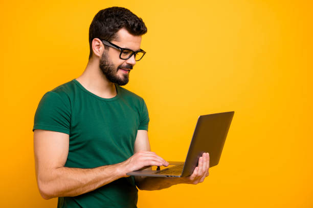 Profile side photo of positive cheerful guy use computer read study work information watch online start-up seminar wear good looking outfit isolated over yellow color background