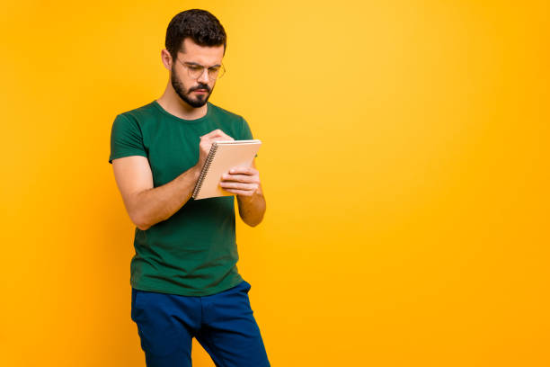 istock Turned photo of concentrated college guy stand copyspace write summary in his copybook wear modern stylish clothing isolated over yellow color background 1207212165