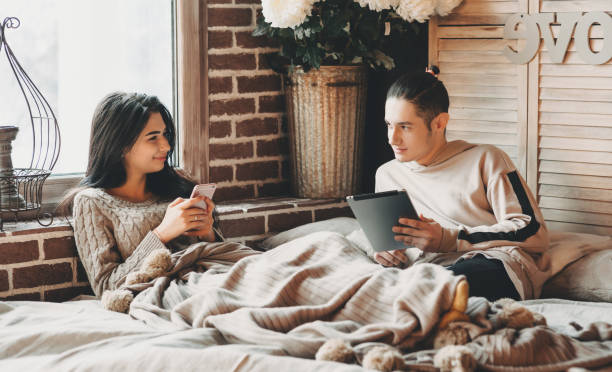 istock Modern caucasian couple spending time in bed using their gadgets and smiling cheerfully at each other 1207212310