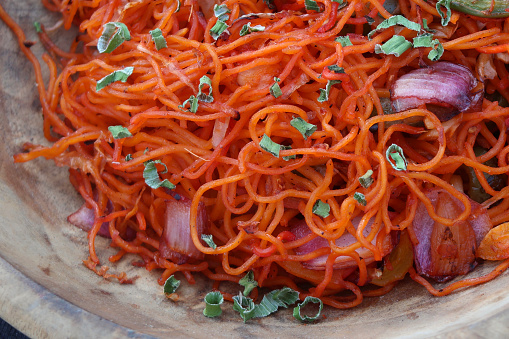 Close-up stock photo showing orange, chinese noodles with red onion, red, green and yellow bell peppers and garnished with spring onion.