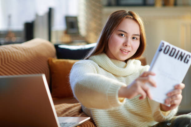 istock happy teen girl with laptop showing educational coding book 1207215827