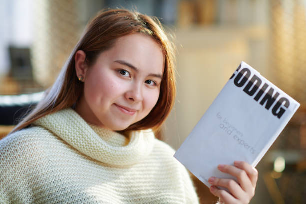 istock smiling modern teenage girl showing educational coding book 1207217505