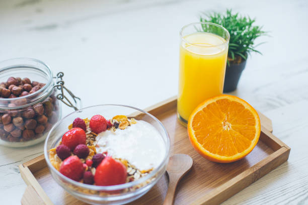desayuno de granola con bayas rojas frescas, naranja, avellanas y jugo de naranja - yogurt yogurt container strawberry spoon fotografías e imágenes de stock