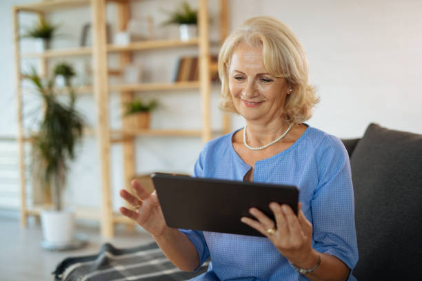 istock Smiling senior woman using digital tablet in living room 1207219430