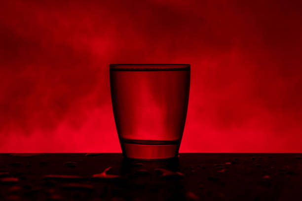 istock Glass with water on wooden table in front red background and smoke 1207220830
