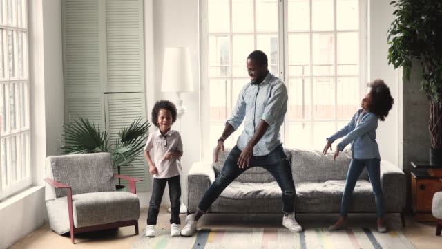 African dad dancing having fun with kids in living room