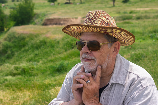 Outdoor portrait of happy Ukrainian countryman in straw hat and sunglasses against hilly spring pasture