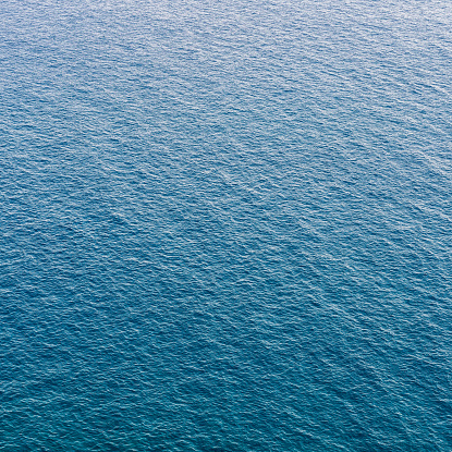 An aerial view of distant waves and ripples on a large surface of blue sea.