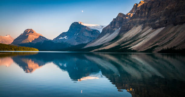 Bow Lake at sunset in Alberta, Canada Bow lake in the Canadian Rockies at sunset. Reflections of the surrounding mountain peaks on the calm water surface. Crowfoot mountain in the foreground. Banff National Park in Alberta - Canada calm water stock pictures, royalty-free photos & images