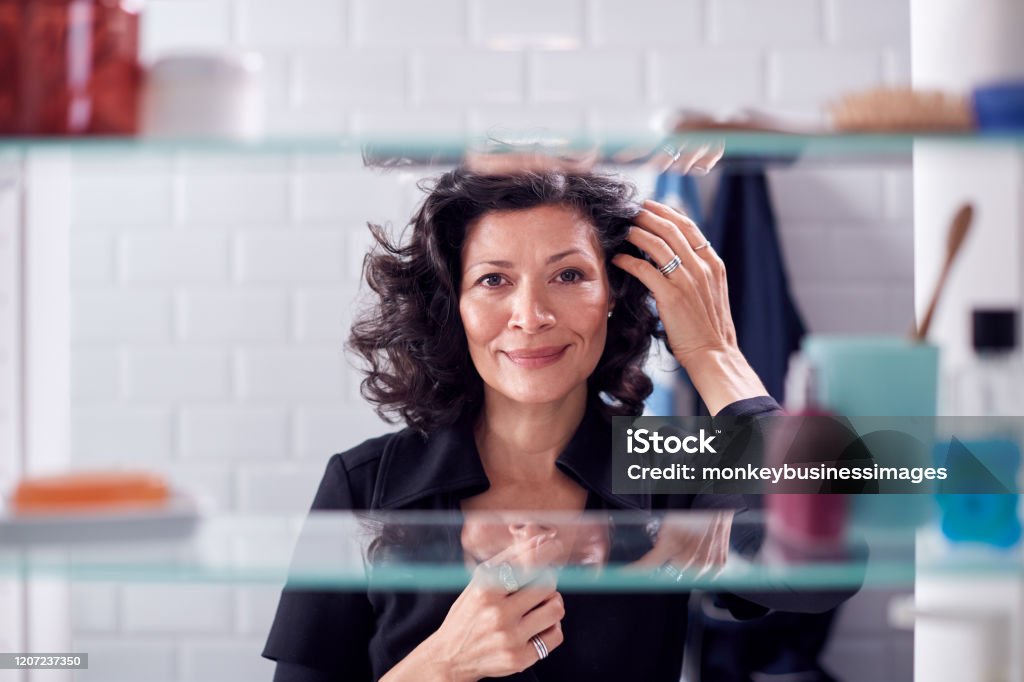 View Through Bathroom Cabinet Of Mature Businesswoman Getting Ready For Work Checking Hair Mature Women Stock Photo