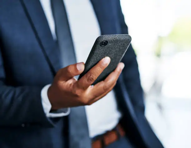 Cropped shot of an unrecognizable businessman using a smartphone while standing in a modern office