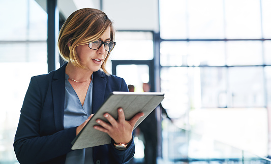 Cropped shot of an attractive young businesswoman using a digital tablet in an office with her colleagues in the background