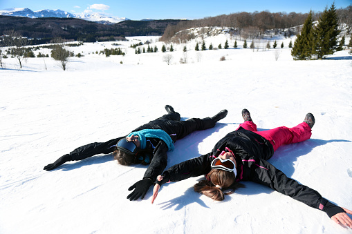 Happy women lying on snow and making angel with arms and legs