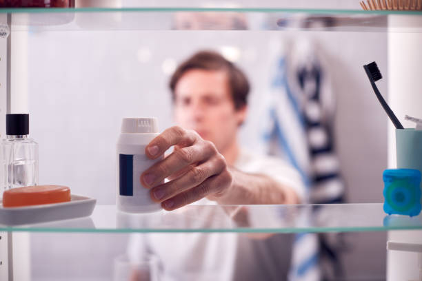 コンテナから薬を服用している男の浴室キャビネットを通して見る - medicine cabinet 写真 ストックフォトと画像