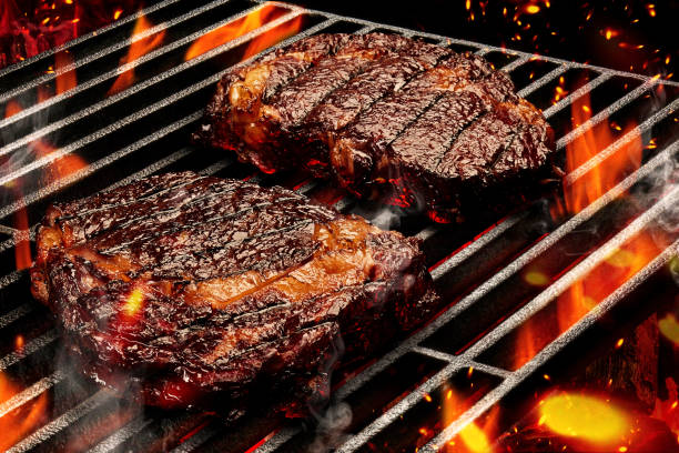 process of preparing two pork or beef steaks. meat roasted on metal portable barbecue bbq grill with bright flaming fire and ember charcoal. close up - steak meat barbecue grilled imagens e fotografias de stock