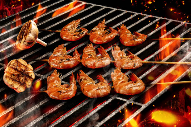 バーベキューバーベキューグリルニンニクの半分と木製の串においしいローストエビを焼きます。炎の火と残り炭。シーフード、貝類。クローズアップ - shrimp grilled prepared shrimp barbecue ストックフォトと画像