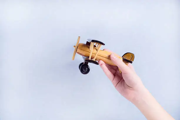 A child's hand with a handmade wooden airplane on a blue background. A child's hand with a handmade wooden airplane on a blue background.