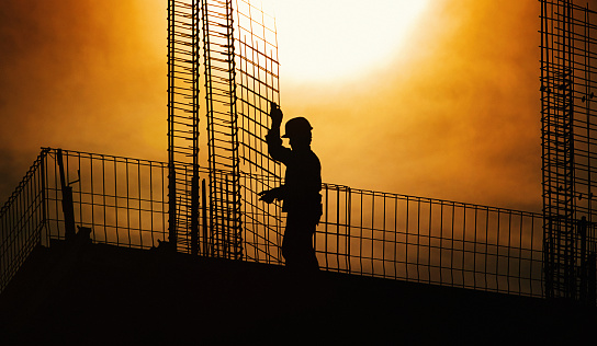 Closeup silhouette of construction worker working on top of a building. Shot against direct afternoon sunlight, workers unrecognizable.