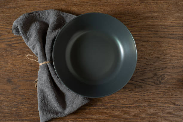 Flat lay, Empty dark black plate with napkin. Black kitchen utensils set on wooden table. Top view with copy free space.