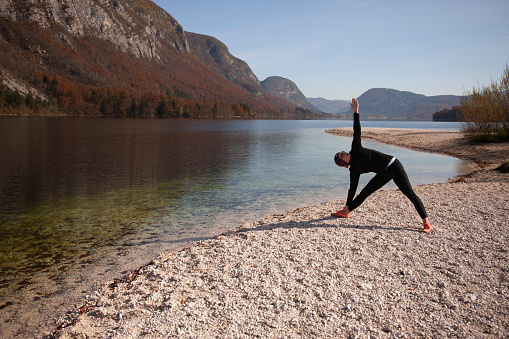 Young woman relaxing by the lake, practicing yoga in a morning light, watching the beautiful view