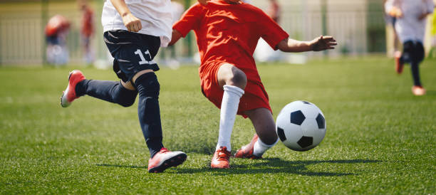 Sports players in football duel run. Footballers running fast and kicking soccer ball on grass stadium during school tournament match. Competition between defender and forward football players Sports players in football duel run. Footballers running fast and kicking soccer ball on grass stadium during school tournament match. Competition between defender and forward football players foul stock pictures, royalty-free photos & images