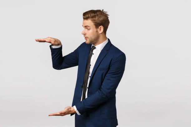istock Impressed handsome bearded blond guy in blue classic suit, shaping big object, talking about business graphs, discuss large product, holding something vast, white background 1207259049