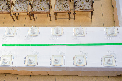 Aerial view to the long served table with plates, glasses, napkins and chairs