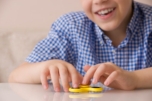 Closeup of child's hands spinning a fidget spinner device. Smiling boy playing with a yellow hand spinner fidget toy